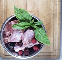 a bowl of meat and berries on a cutting board