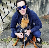 a man in sunglasses kneeling down with a dog on a leash